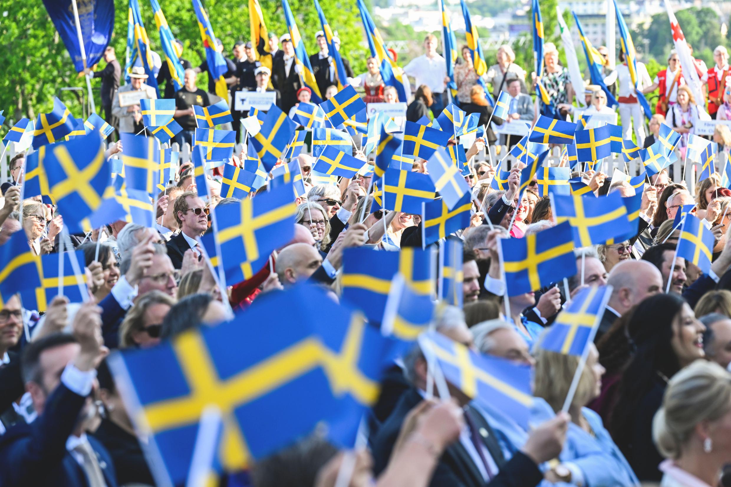 A crowd of people waving Sweden's blue and yellow flag.